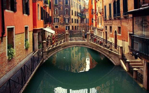 A historic bridge over a calm canal in Venice with classic old buildings lining the waterway
