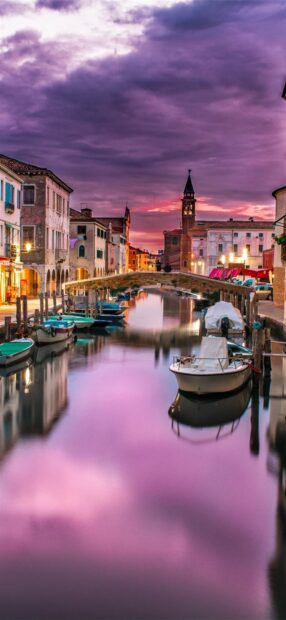 Historic Venice canal with boats at sunset reflecting purple sky