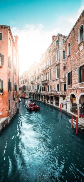 A Venice canal with a boat passing between historic buildings under a bright sky