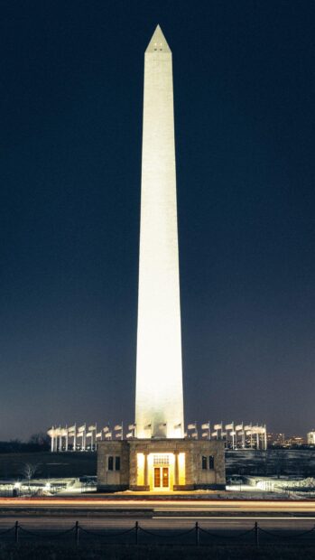 Washington monument in Washington Dc illuminated at night with flags around the base