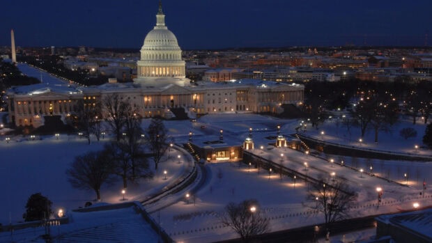 Washington Dc snow covered Capitol building at night with glowing lights in the cityscape