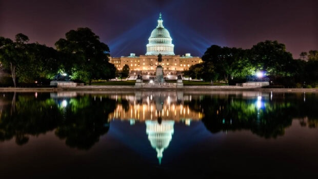 The Washington Dc building reflecting on the water at night with bright lights and surrounding trees
