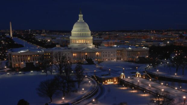 The united states capitol building with lights on in Washington Dc at night covered in snow
