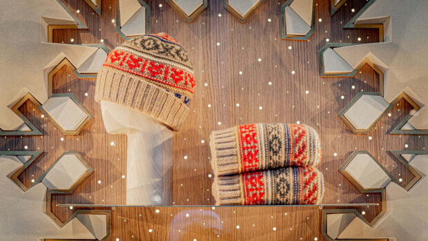 Knitted winter pattern hat and gloves displayed on a wooden texture with decorative lights