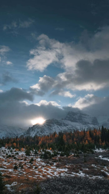 Winter landscape with snow covered mountains and colorful trees under cloudy sky