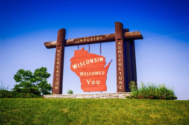 Wooden Wisconsin welcome sign on a grassy hill under a clear blue sky