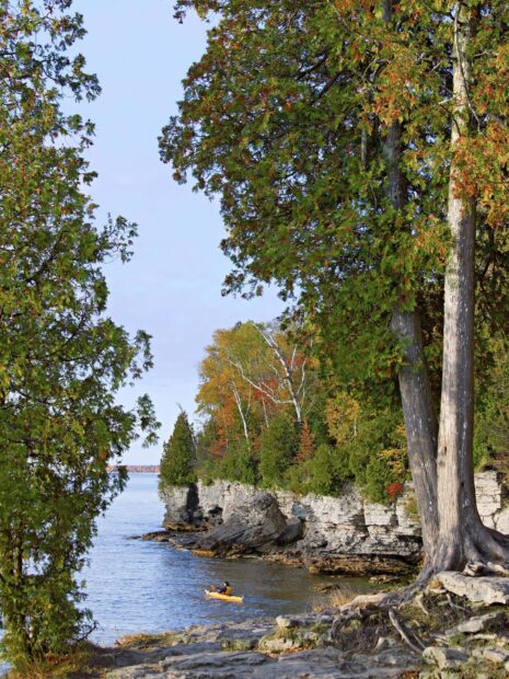 Person kayaking near rocky cliffs and autumn trees in Wisconsin lake
