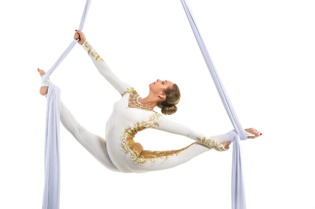 Aerial silks artist performing a complex pose in a white and gold costume