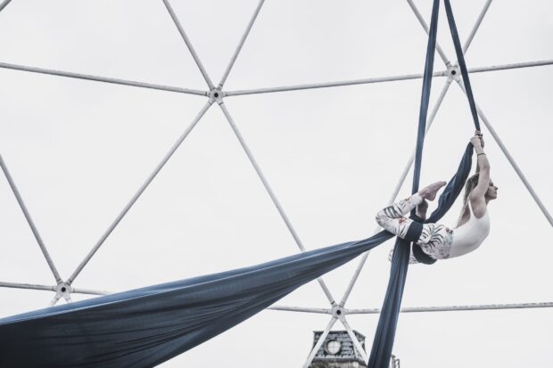 Aerial silks artist performing a graceful pose suspended in the air on blue silks