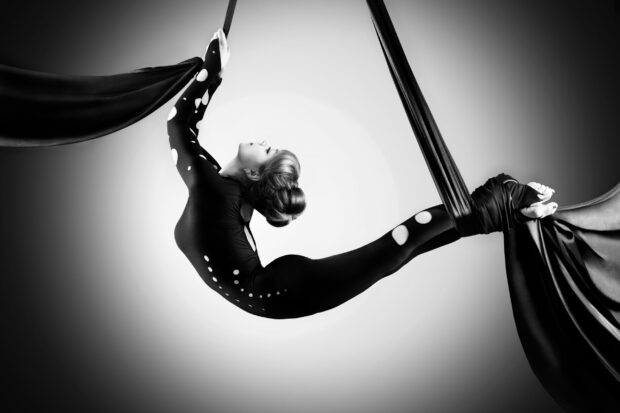 Aerial silks artist performing a midair pose with long black fabric