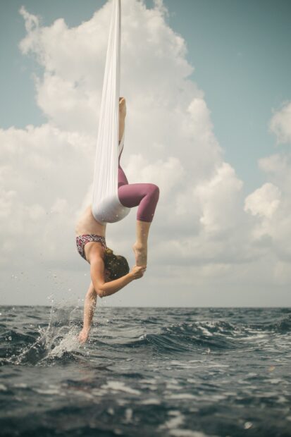 A woman performing aerial silks over the ocean while touching the water with her hand