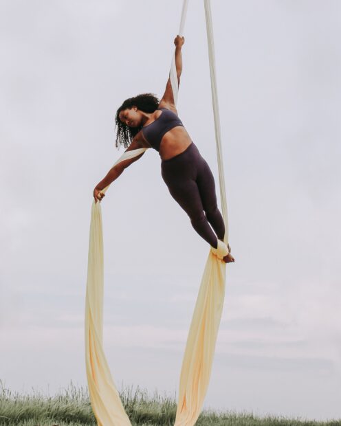 A woman performing aerial silks balancing with yellow fabrics outdoors