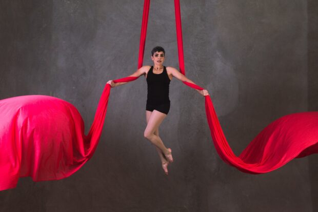 Aerial silks artist performing with flowing red fabrics against a gray wall