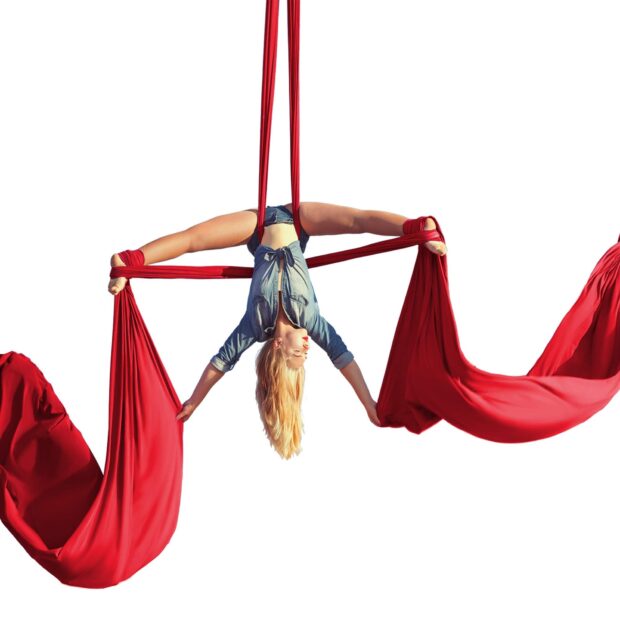 Flexible aerial silks performer stretching on red fabric in innovative pose