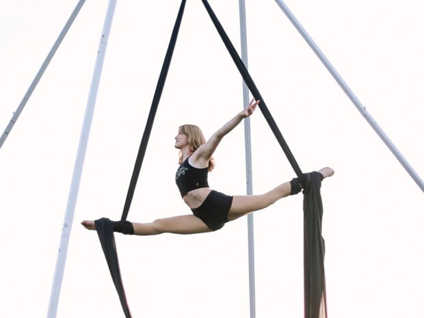 A woman performing aerial silks split pose suspended in midair