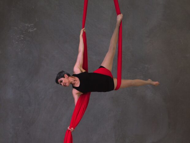 A woman practicing aerial silks performing a horizontal pose with red fabric in a studio