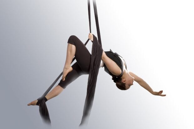 A woman practicing aerial silks performing an advanced pose using aerial silks