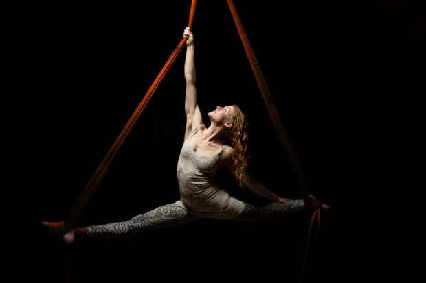 Aerial silks artist performing a split while suspended by fabric