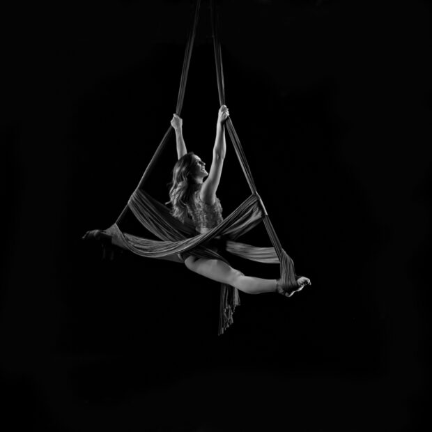 Aerial silks artist performing a split while suspended in the air on fabric