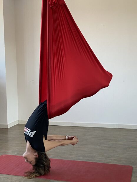 A woman practicing aerial silks exercise hanging upside down with red fabric