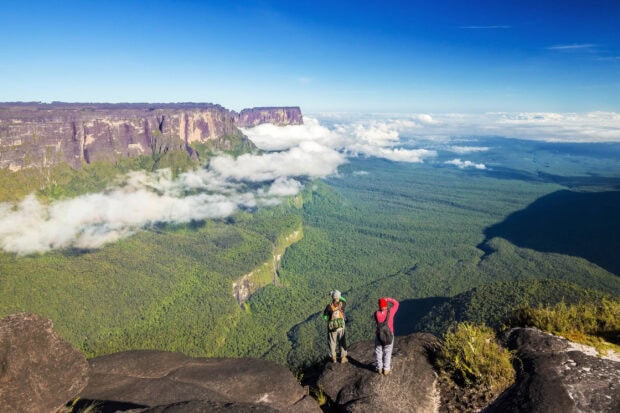 Two hikers enjoy the Canaima National Park view from the cliff edge