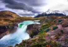A scenic landscape of Canaima National Park featuring a powerful waterfall surrounded by lush vegetation and mountains