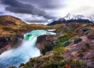 A scenic landscape of Canaima National Park featuring a powerful waterfall surrounded by lush vegetation and mountains