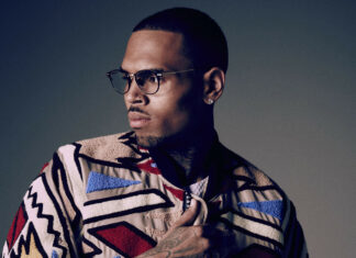 Chris Brown wearing glasses and a colorful jacket looking to the side in a high quality portrait