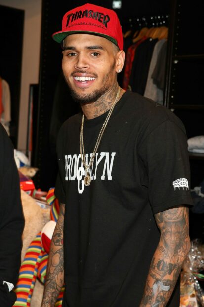 Chris Brown wearing a red Thrasher cap and black Brooklyn t shirt smiling with visible tattoos