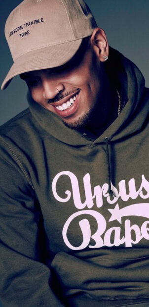 Chris Brown wearing a hooded sweatshirt and cap smiling warmly