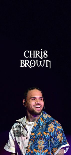 Chris Brown smiling in a colorful shirt with braided hair on stage under bright lights