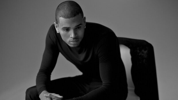 Chris Brown wearing a black shirt sitting thoughtfully on a chair in a black and white setting