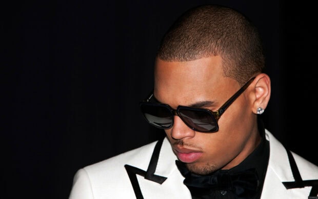 Chris Brown wearing sunglasses and a white suit with a black bow tie in a close up portrait
