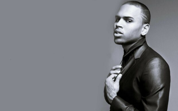 Chris Brown with tattooed hand adjusting his leather suit jacket in a black and white photo