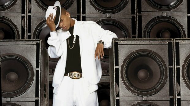Young Chris Brown wearing white outfit and holding hat in front of speakers