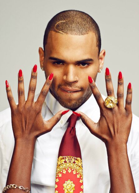 Chris Brown showing red nails and a large gold ring while wearing a red and gold tie