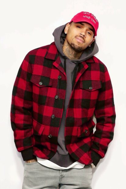 Chris Brown wearing a red and black checkered jacket and a red cap standing against a white background