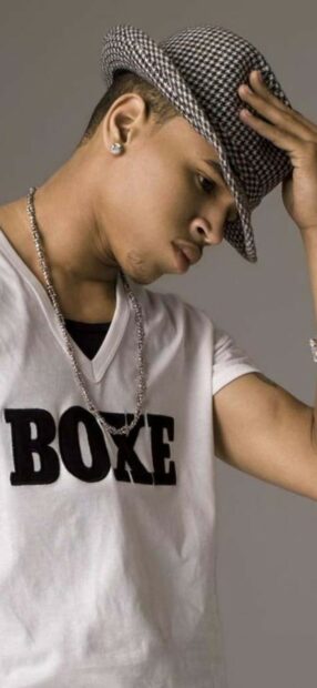 Young Chris Brown wearing a patterned fedora and white shirt with a chain necklace