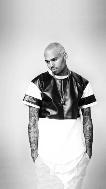 Chris Brown standing with tattooed arms looking down in a black and white shirt