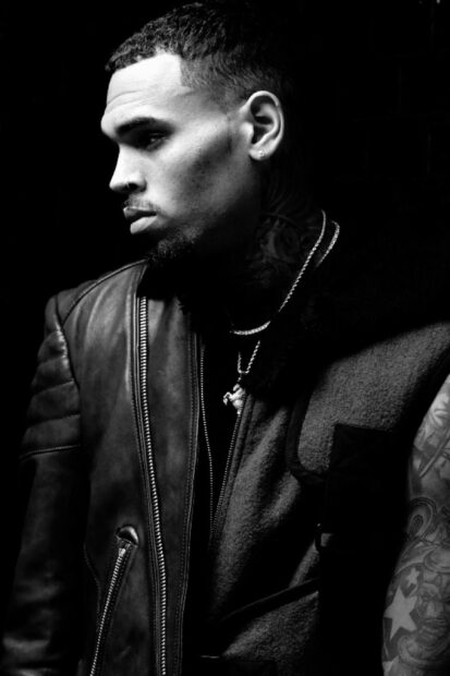 Chris Brown wearing a leather jacket with tattoos visible on his arm in a black and white portrait