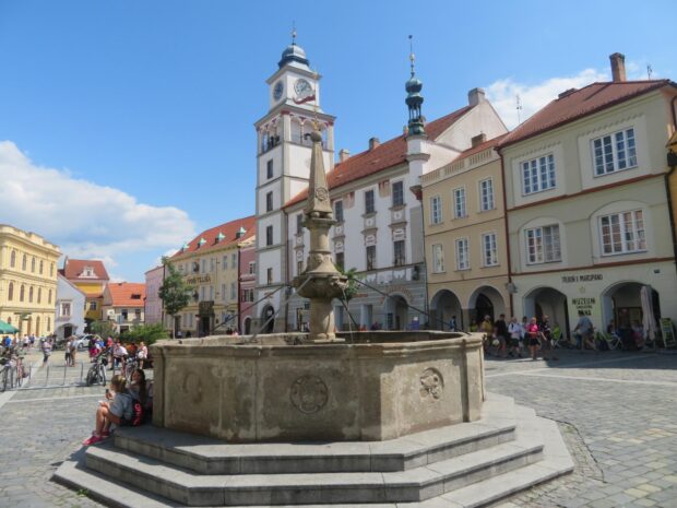 Historic city square with stone fountain and clock tower under a clear blue sky