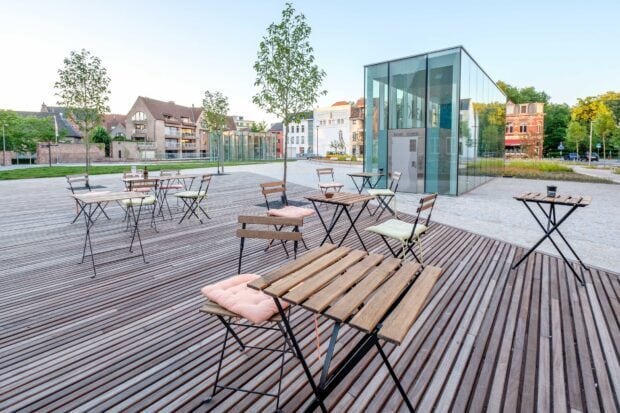 Modern city square featuring wooden tables and chairs with a glass building in the background