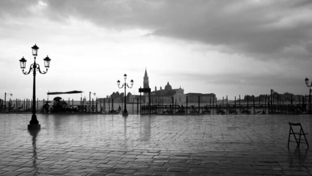 City square with old street lamps and gondolas by the waterfront under cloudy sky