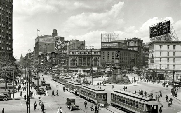 Historic city square bustling with vintage streetcars and early 20th century buildings in black and white