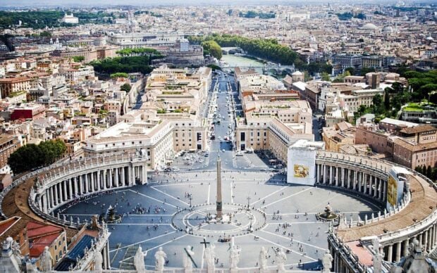A bustling city square with historical buildings and stone statues in a European cityscape