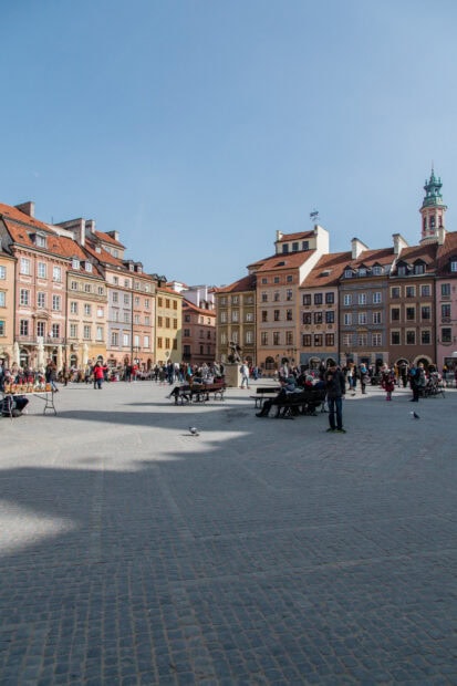 Historic city square filled with people and colorful buildings under clear blue sky