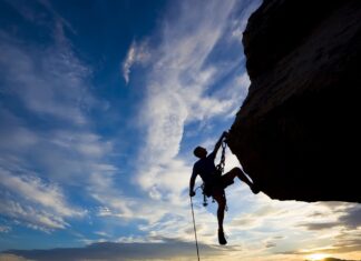 A climber ascending a rocky cliff with climbing gear against a blue sky