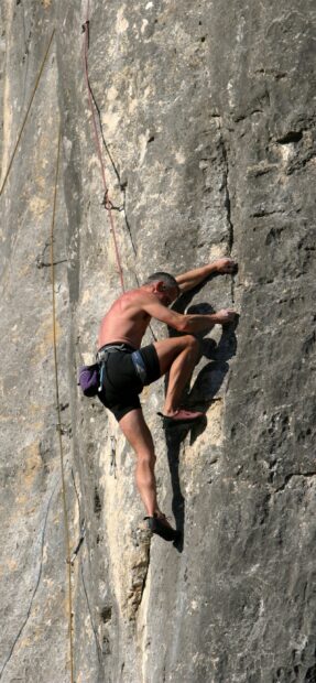 Man climbing a steep rock wall with climbing gear in a challenging outdoor setting