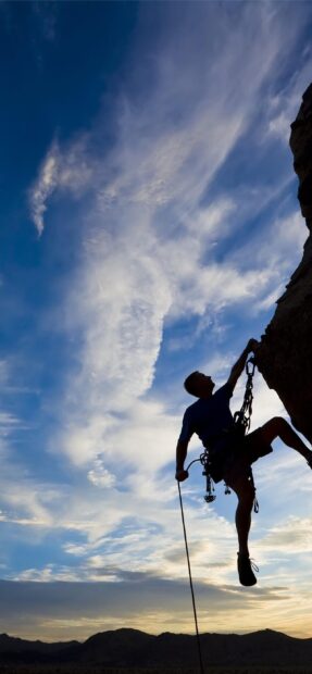 A climber scaling a steep rock face against a vivid sky during sunset