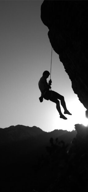 A climber descending a cliff with a rope against a mountain landscape at sunset